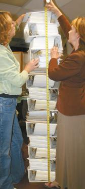 Staff of The Mountain Enterprise, (left) Office Manager Pam Sturdevant and (right) Managing Editor Patric Hedlund measure a simulation of the nearly six-foot tower of 21,000 pages  known as the Tejon Mountain Village Draft Environmental Impact Report?thirteen 5.5-inch notebooks, two 2-inch notebooks and two large rolled maps. 
The public has been given only until July 13 to read, digest, analyze and comment upon the document?that is, if it were available. Kern County has only three full sets of the DEIR total, and those are all in Bakersfield.

