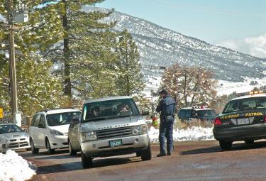 Here a CHP officer at the base of Mount Pinos explains safety requirements to snow visitors. On February 27 cars were parked close together, and a 5-year-old child ran onto the roadway into a CHP vehicle that was traveling about 15-20 miles per hour, witnesses said. [Hedlund Photo/The Mountain Enterprise]