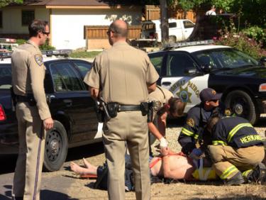 CHP officers stand by as their fellow officer adjusts handcuffs on the suspect's wrists on Circle Drive. Kern County Fire Station 57 crew members provide medical aid to the suspect. [photo by The Mountain Enterprise]