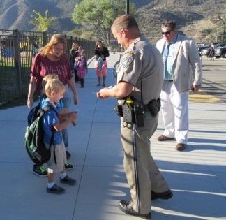 Student Terry Henderson receives his Junior Officer badge from Fort Tejon Officer Brian Moore on the first day at Frazier Park Elementary School. Officer Moore and Principal Chuck Mullen were there to greet students as they arrived. [photo by Gary Meyer, The Mountain Enterprise]