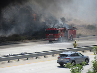 A Los Angeles County firefighter puts water on a burning tire in the center divider of I-5 just seconds before an explosion from the burning truck sent debris flying toward him. He was able to jump out of the way. [photo by Gary Meyer, The Mountain Enterprise]