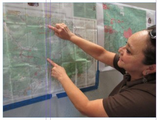 Helen Tarbet, an information officer with the Los Padres National Forest, shows the location of Pine Mountain Club with her right hand and the location of the fire with her left. As the crow flies, the fire was about 16 miles southwest of the Mountain Communities [update: by Monday, July 4 it was 13 miles from Pine Mountain Club]. The topography in the Sespe Wilderness Area is rugged and steep. The real distance is  greater, but the fire is not contained. The spread of the fire is toward the northeast. [Patric Hedlund photo for The Mountain Enterprise].