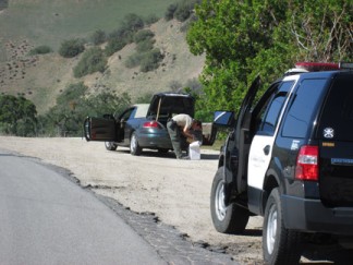A Los Angeles County Sheriff's deputy searches the trunk of a stolen vehicle on Lebec Road while the suspects are in custody in the back of a patrol vehicle. [photo by Gary Meyer]