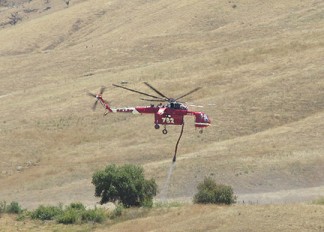 An Erickson sky-crane helicopter lifts off after loading up with water just south of Jack In The Box at Grapevine. [photo by Gary Meyer, The Mountain Enterprise]
