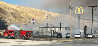 Photo by Gary Meyer, The Mountain Enterprise. An LA County Firefighter puts water on a burning wood structure just 150 yards north of McDonalds in Gorman, at about 4 p.m. on June 15.